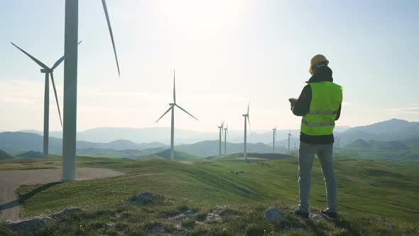 Technician Engineer in Wind Turbine Power Generator Station Standing with a Tablet in His Hands