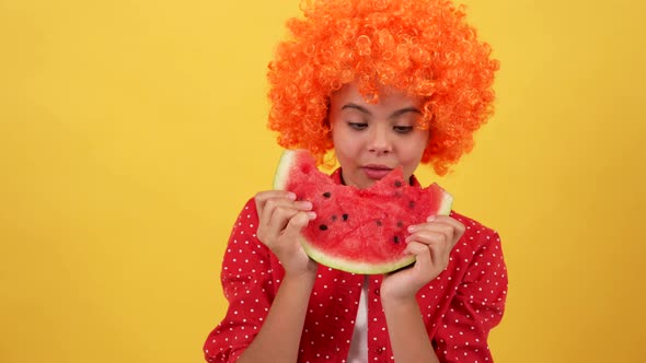 Amazed Hungry Child in Fancy Orange Hair Wig Eat Water Melon Slice on Yellow Background Hunger alt