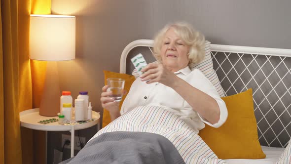 Sick Senior Woman Taking Medicines and Drinking Water While Lie on Bed