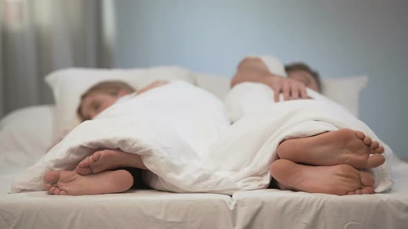 Young Man and Woman Sleeping Back to Back, Scratching Feet, Fungal Disease alt