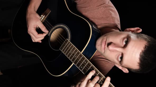 Vertical video Young man plays an acoustic guitar on a black background alt