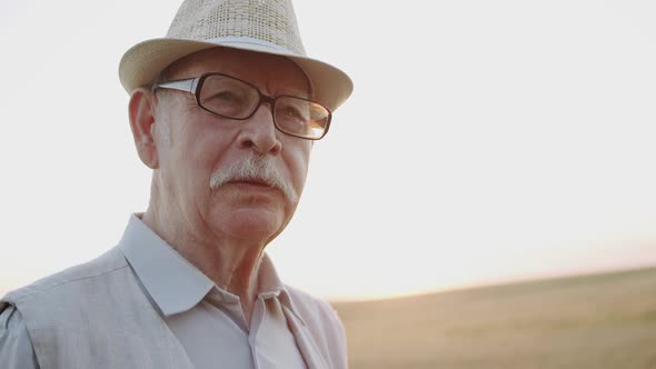 Portrait of Senior Man Eats Fresh Bread and Has Pleasure in Sunny Wheat Field alt
