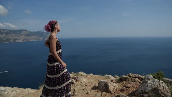 Girl in a Long Dress Stands on Top of a Mountain and Looks Into the Distance alt