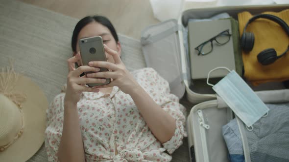 Asian female lying on the floor in bedroom typing message on social media. alt