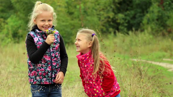 Two beautiful little girls happily sniffing a bouquet of wild flowers outdoors