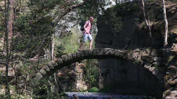 Man With Backpack Walking Across Old Stone Bridge Over River