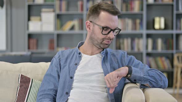 Portrait of Anxious Young Man Waiting and Checking Smart Watch alt