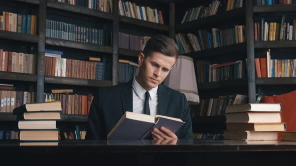 Businessman in Classical Suit Sitting in Library Reading Book