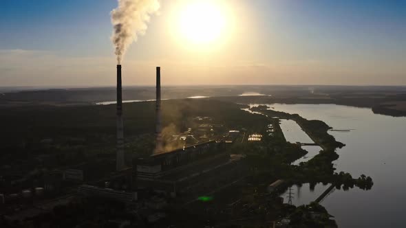 Dark factory against the orange setting sun. Factory pipes with smoke.  alt