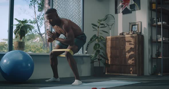 African American Male Doing Physical Exercise with Elastic Bands at Home