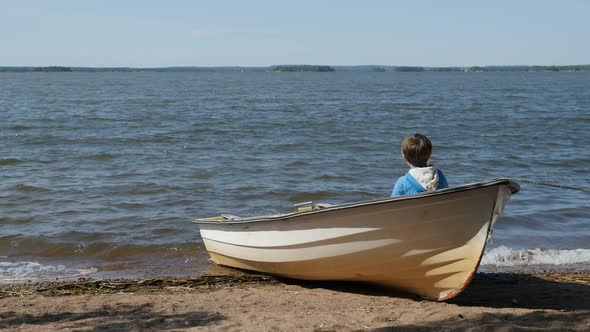 Little Boy Sitting In Wooden Fishing Rowboat Beached On Sandy Beach