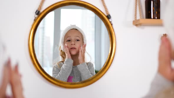 Little Girl Applying Creme on Face with Mother alt