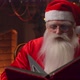 An Elderly Man with a White Beard in a Santa Claus Suit Sitting in a Chair Against the Background - VideoHive Item for Sale