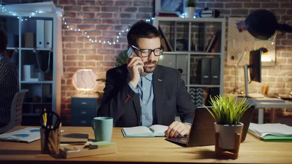 Cheerful Guy Chatting on Mobile Phone in Office in the Evening Discussing Work alt