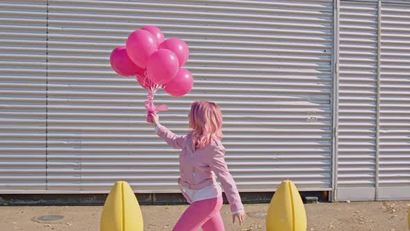 Happy woman with pink hair holding pink balloons running in the street alt