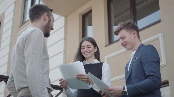 Portrait Three Young Employees Are Discussing a Project While Holding Papers or Documents Outdoors alt