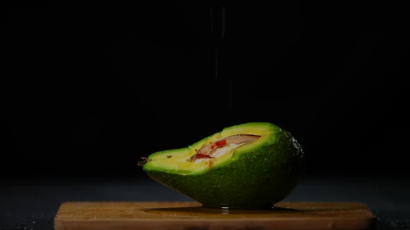 White Salt Falling in Slow Motion on Green Avocado Covered with Olive Oil alt