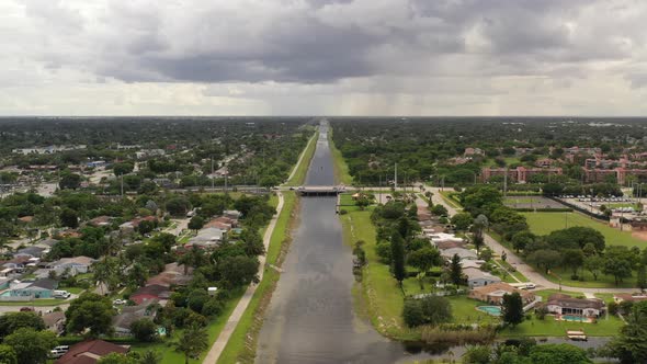An aerial view of a long canal on a cloudy day. The camera dolly in over the water towards an overpa alt