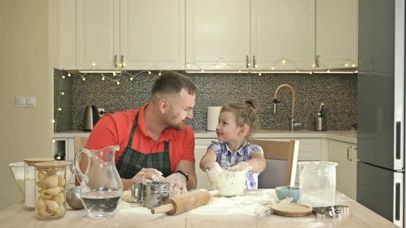 Dad and Daughter 5-6 Years Old Knead Dough in the Kitchen. The Father Treats His Child with Great alt