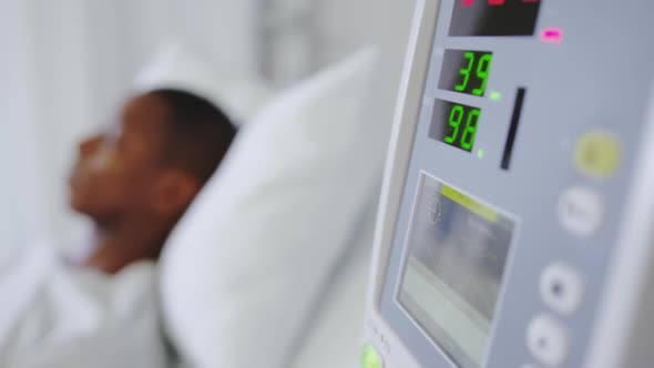 Close-up of medical monitor with African american male patient in the ward at hospital alt
