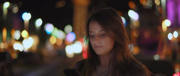 A young woman listening to the music on her phone in the middle of a street alt
