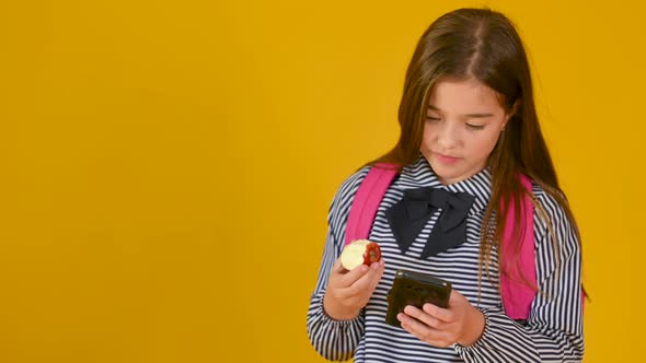 Portrait of a schoolgirl with a backpack eats an apple and communicates on social networks. alt