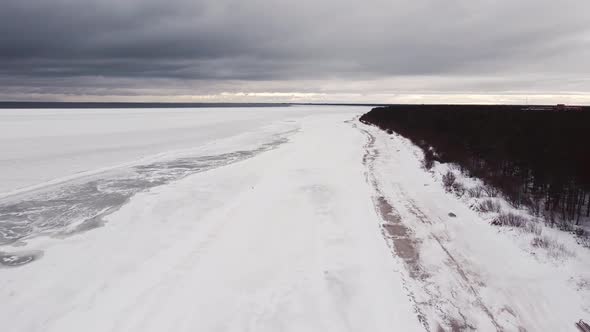 Seascape in winter. Snowy shore, forest and ice covered sea, on gloomy sky background. Air flight