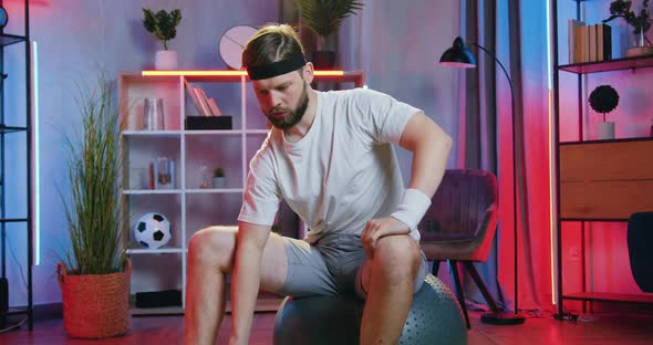 Man in Sportswear Sitting on Fitball and Doing Exercises with Dumbbells to Keep His Body Healthy alt