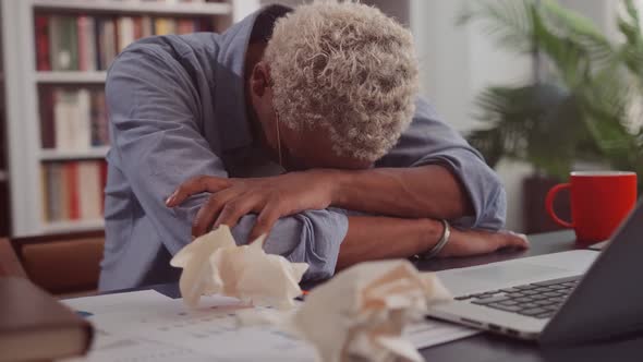 Tired Dark Skinned Man Sleeping at Workplace Placing Head on Documents alt