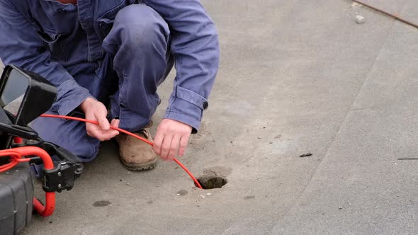 Plumber diagnoses a drain well on the street using special equipment. alt