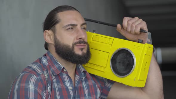 Close-up of Young Caucasian Man with Brown Eyes Listening To Music From Vintage Yellow Tape Recorder alt