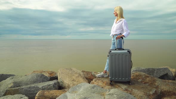 A beautiful woman with a suitcase on the background of the sea alt