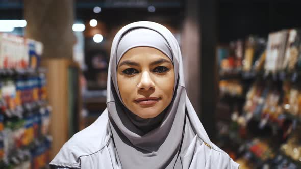 Portrait of Young Beautiful Confident Smiling Muslim Woman with Piercing in Hijab in the Supermarket alt