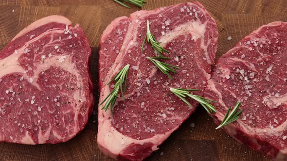 Seasoning raw ribeye beef steaks with rosemary