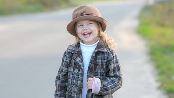Cute little girl in a coat and hat walks on the meadow alt