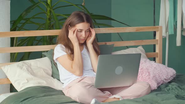 A Young Woman Feels Headache Eye Strain While Working on Laptop in Bed at Home alt