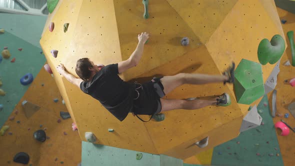 Confident Male Mountaineer Climbing Artificial Rock Wall Indoors in Sportive Center