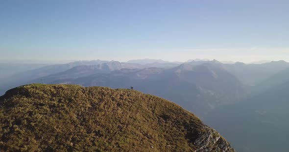 Drone flies far away to show the huge mountain top. Two men are standing on it. alt
