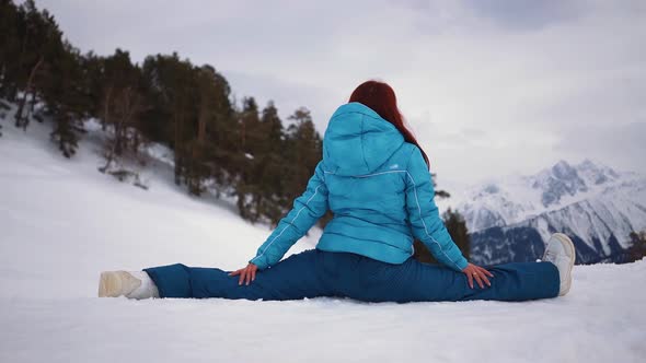 Girl in Skiing Equipment Sits in Splits Against Backdrop Mountain Winter alt