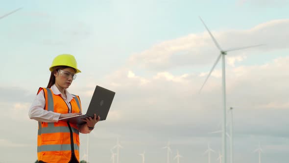 young female engineer working with laptop computer against wind turbine farm