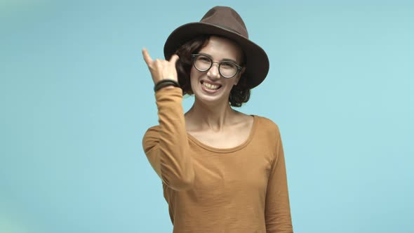 Joyful Girl Tourist in Glasses and Trendy Hat Enjoying Party Showing Rocknroll Gesture and Having