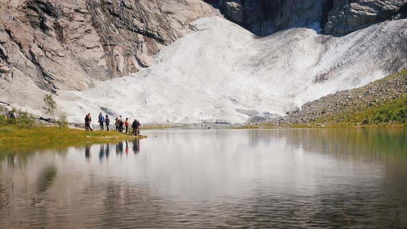 A Group of Tourists Near a Small Lake and a Glacier in Norway. Scandinavian Nature and Tourism alt