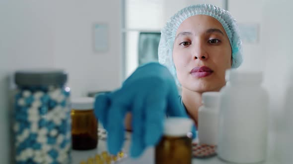 Female Doctor in Medical Uniform Taking Pills from Shelf in Clinic alt