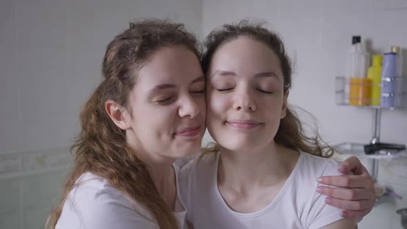 Closeup Charming Beautiful Twin Sisters Hugging Looking at Camera alt