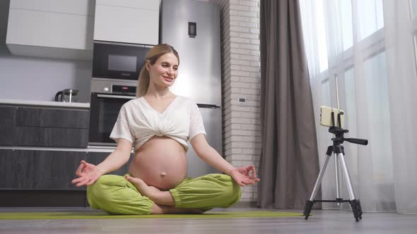 A Pregnant Woman Does Yoga at Home with a Smartphone