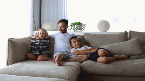 Happy Family with Two Children Reading Book Together in Living Room at Home