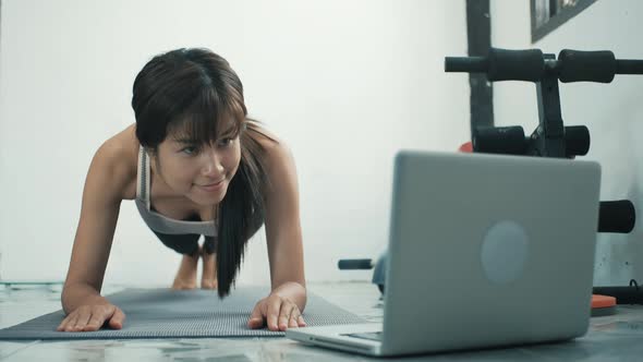 Strong beautiful fitness Young asian woman doing plank exercise and using laptop alt