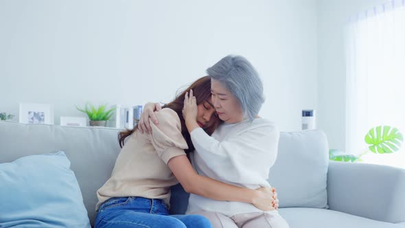 Asian loving elderly mother consoling and comforts upset daughter crying in tears for problem. alt