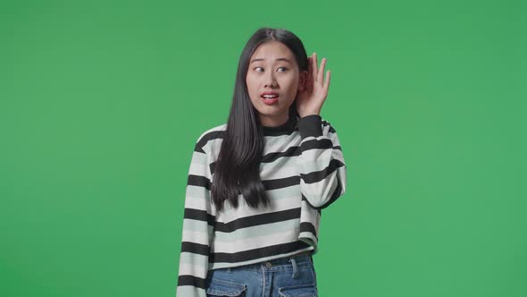 Asian Listening To Something Carefully While Standing In Front Of Green Screen Background alt