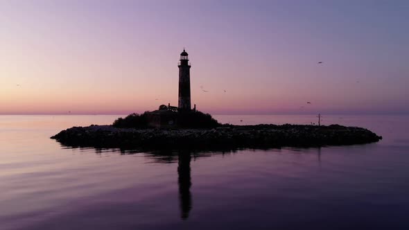 Dark small island and lighthouse tower after sunset, orbiting aerial shot
